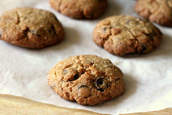 A stack of warm, freshly baked whole wheat vegan chocolate chip cookies with visible melted chocolate chips, presented on a rustic plate.