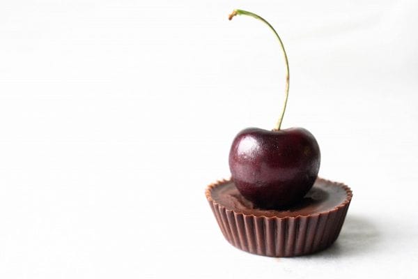 Stack of Raw Dark Chocolate Cherry Cream Cups, showcasing the rich chocolate shell and vibrant pink cherry cream filling inside.