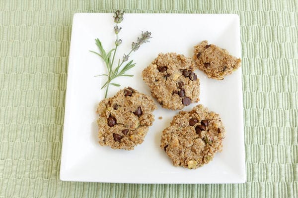A stack of golden-brown vegan Quinoa Lavender Cookies, studded with pistachios and non-dairy chocolate chips, resting on a cooling rack.