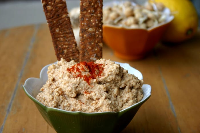 Creamy Raw Sprouted Hummus in a bowl, garnished with paprika and olive oil, served with fresh vegetable crudites and crackers.