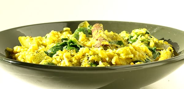 A vibrant bowl of vegan Kitcheri, garnished with fresh green coriander leaves, showcasing the yellow rice and dal with visible pieces of broccoli and zucchini.