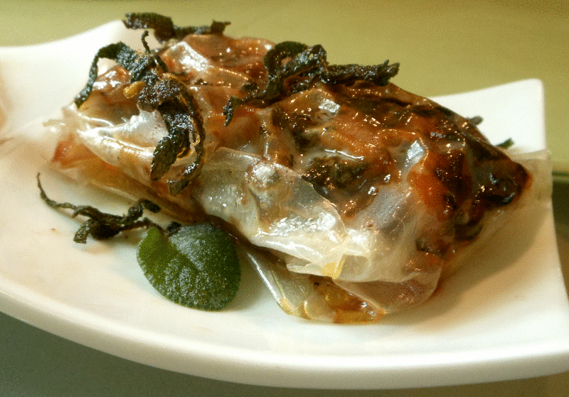 Golden-baked sweet potato spring rolls, drizzled with glistening anise-scented sage-butter sauce and fresh sage leaves, on a white plate.