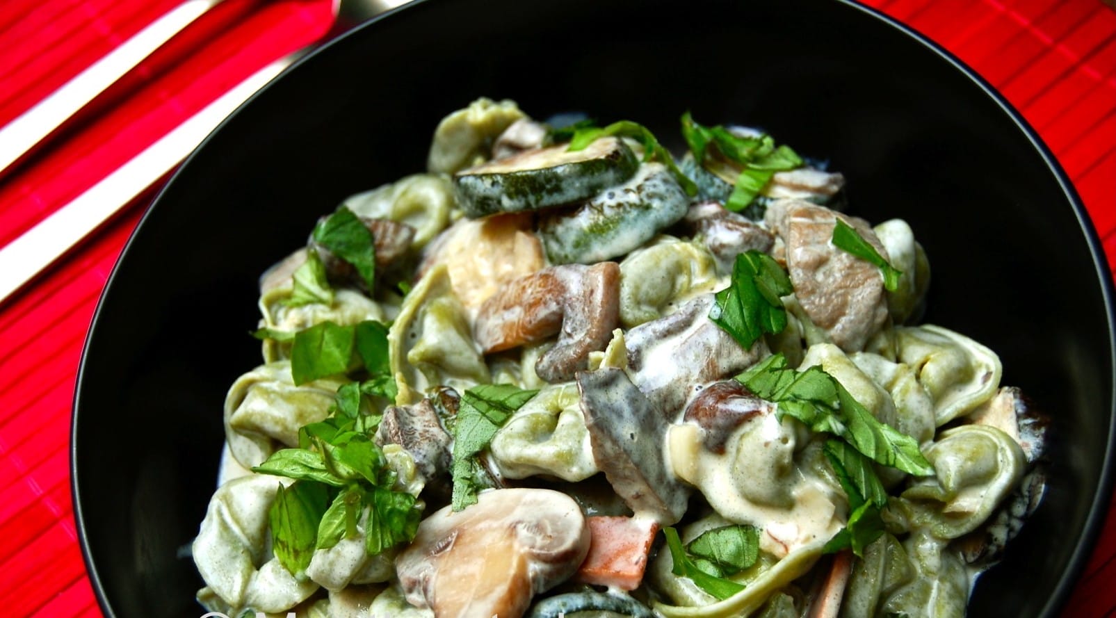 A bowl of vegan tortellini with a creamy wild mushroom and tempeh bacon sauce, garnished with fresh basil and vegan Parmesan.