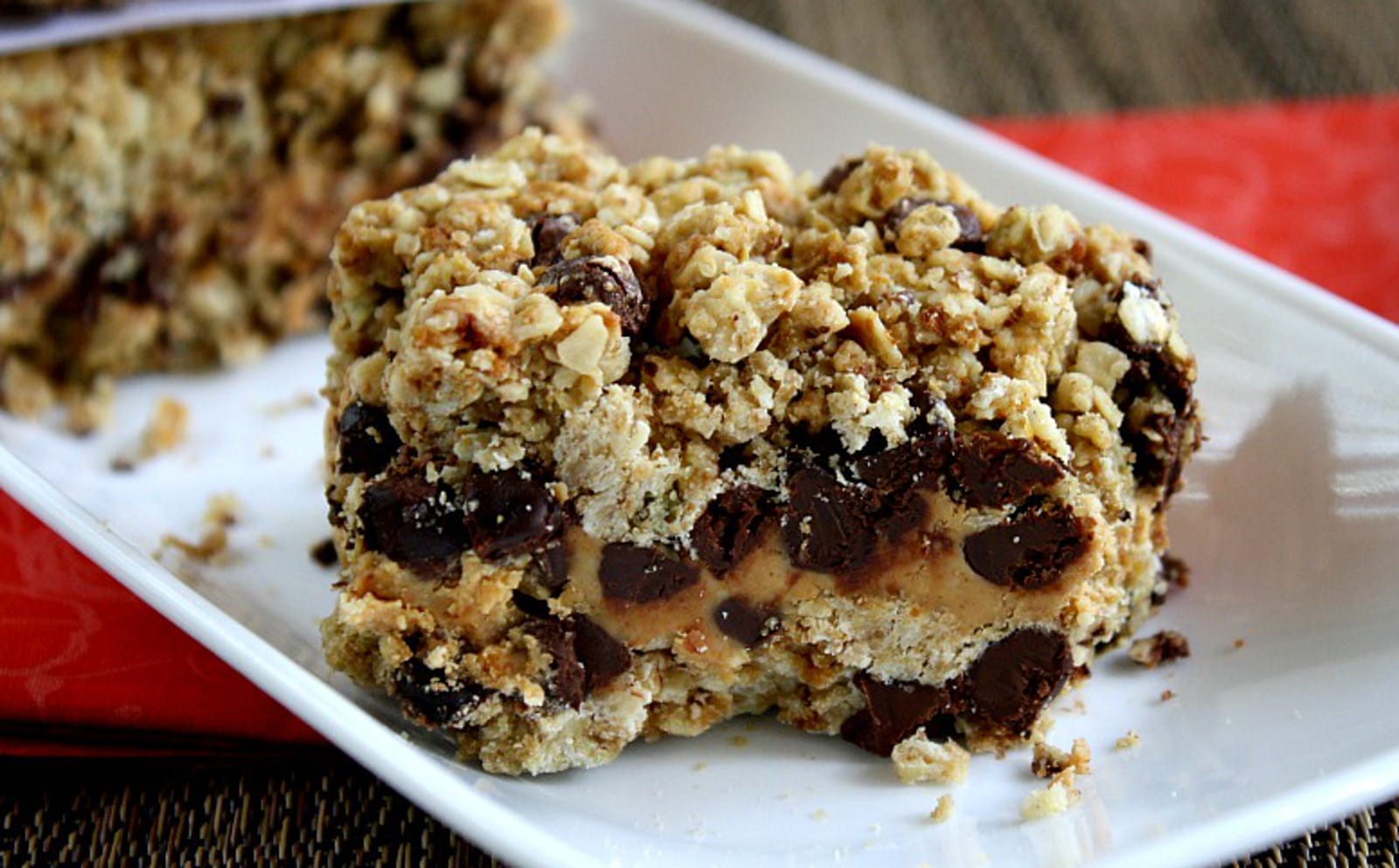Close-up of a stack of three square vegan Peanut Butter and Chocolate Chip Oat Bars, showing the distinct layers of golden oat crust and creamy peanut butter filling with visible chocolate chips.