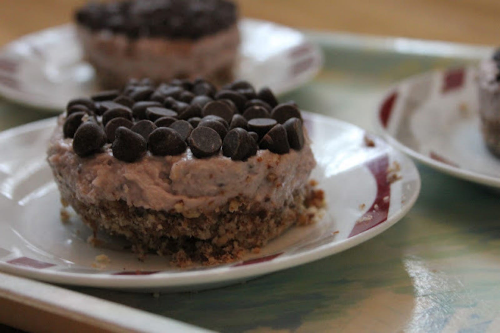 A close-up of two mini individual raw strawberry cheesecakes, removed from their tins, garnished with dark raw cocoa nibs.