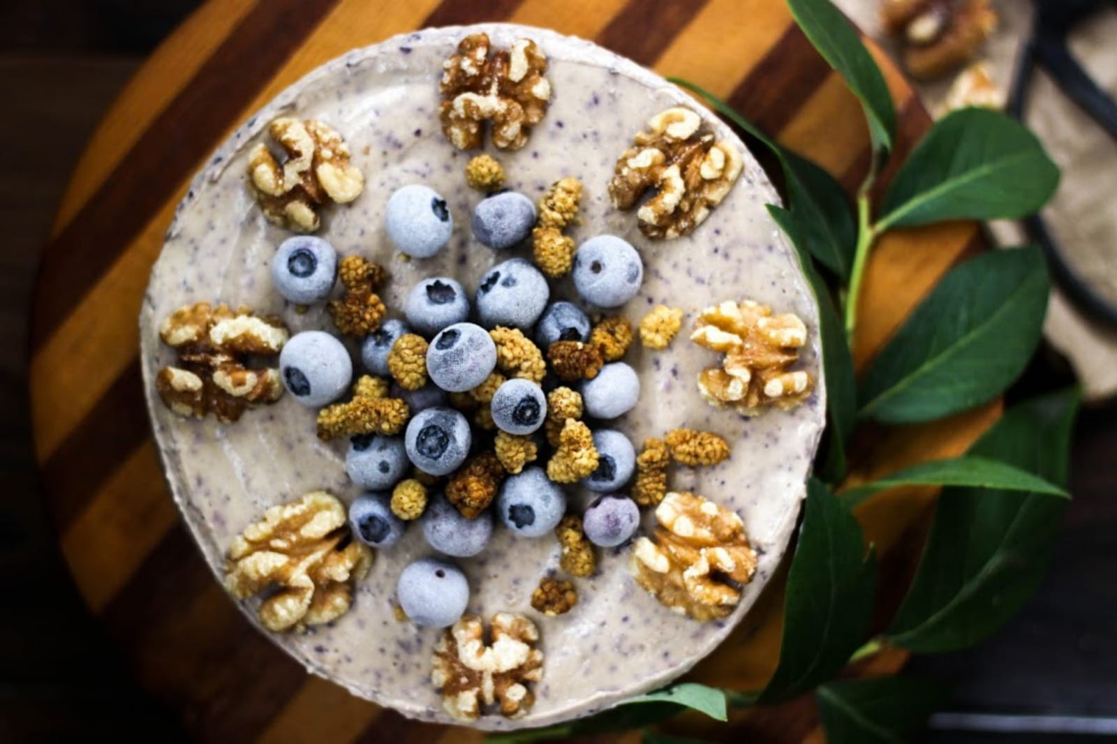 A slice of Raw Blueberry Vanilla Creme Cake on a white plate, revealing its distinct oat-date crust, creamy vanilla cashew layer, and vibrant blueberry top layer, garnished with fresh blueberries.