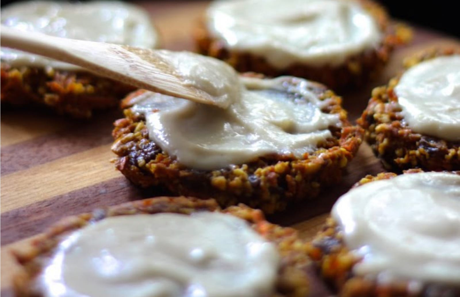 A stack of round, golden-brown Carrot Cake Cookies, generously topped with a swirl of creamy white Lemon Cream Frosting, garnished with a sprinkle of cinnamon.