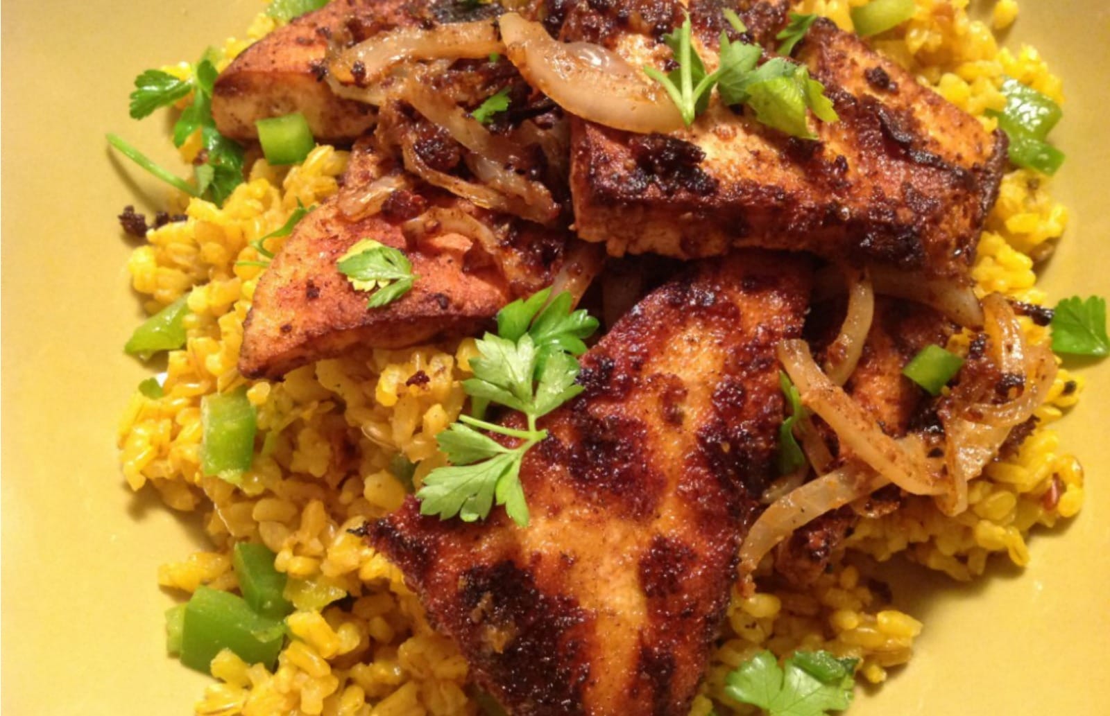 Plated Chile-Rubbed Tofu and Onions over a bed of Spanish brown rice, garnished with fresh cilantro and a lime wedge.