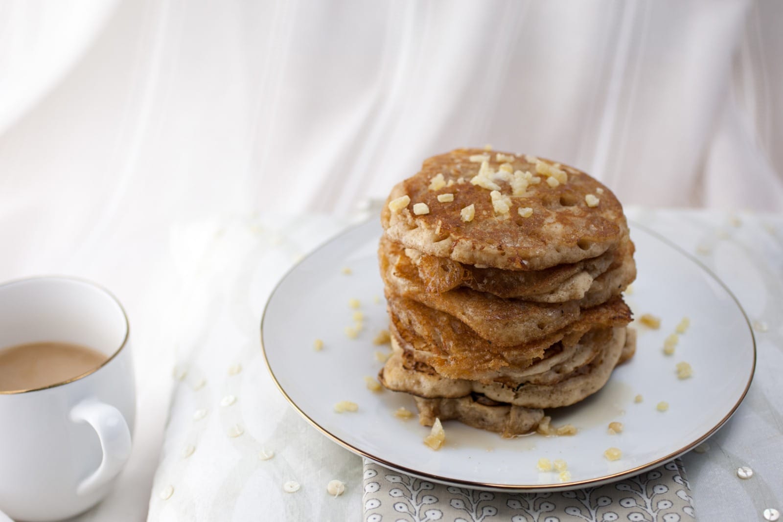Stack of golden-brown vegan maple ginger pancakes, drizzled with maple syrup, topped with vegan butter and chopped candied ginger.