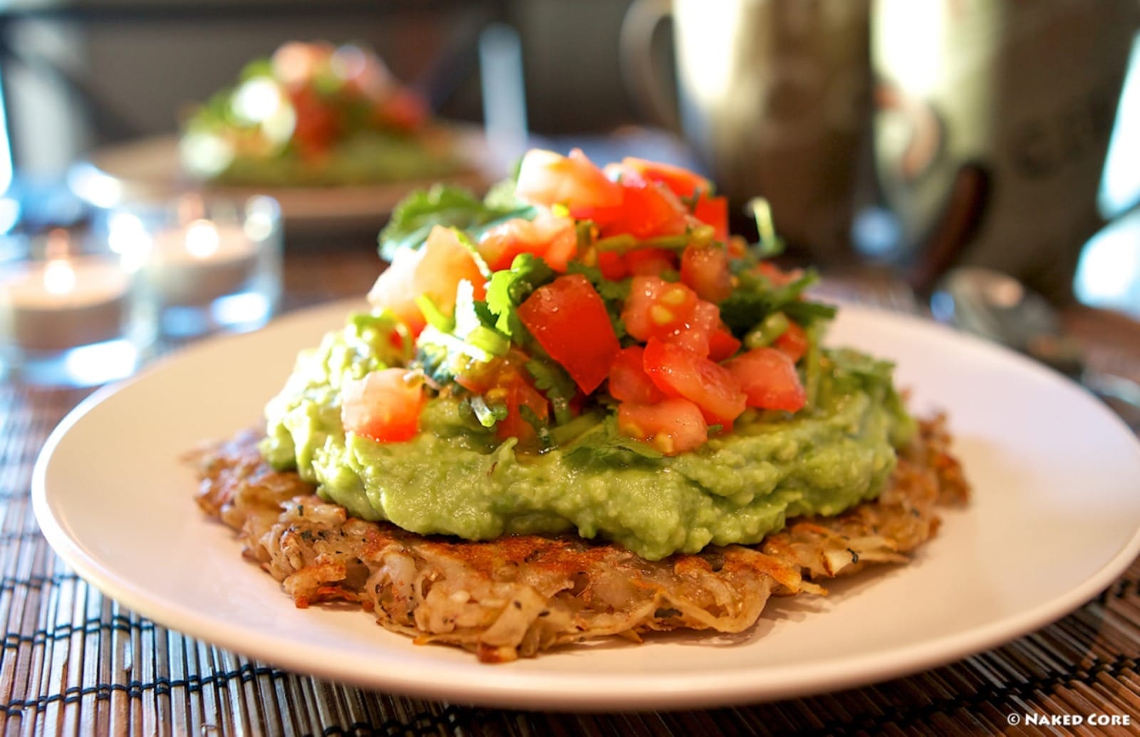 Golden-brown vegan potato hashcakes stacked, topped with creamy green guacamole and a vibrant red tomato-cilantro salsa, served on a plate.