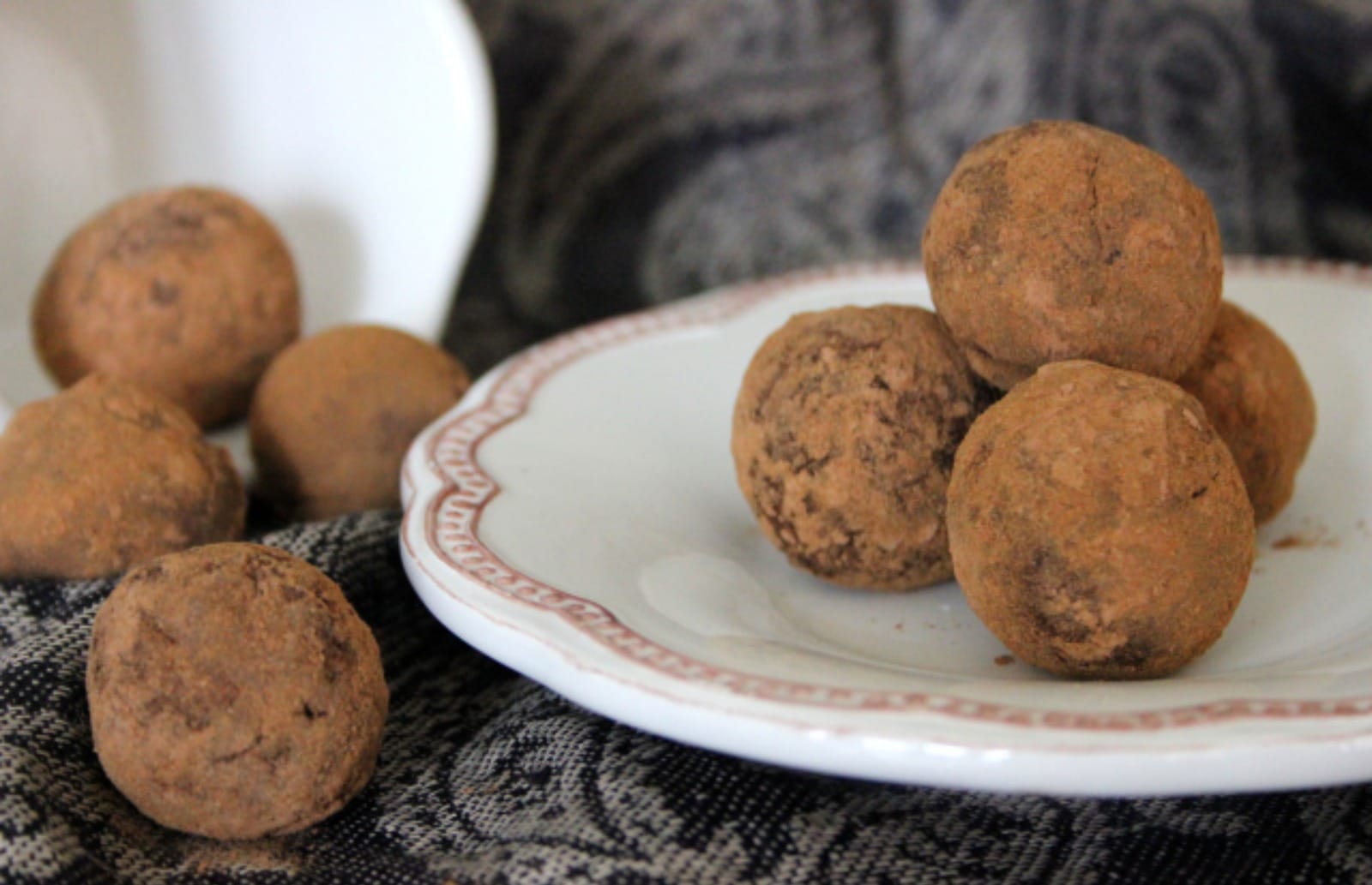 A small pile of round Raw Cinnamon Chocolate Truffles, coated in a dark brown cacao and cinnamon powder, arranged on a light plate.
