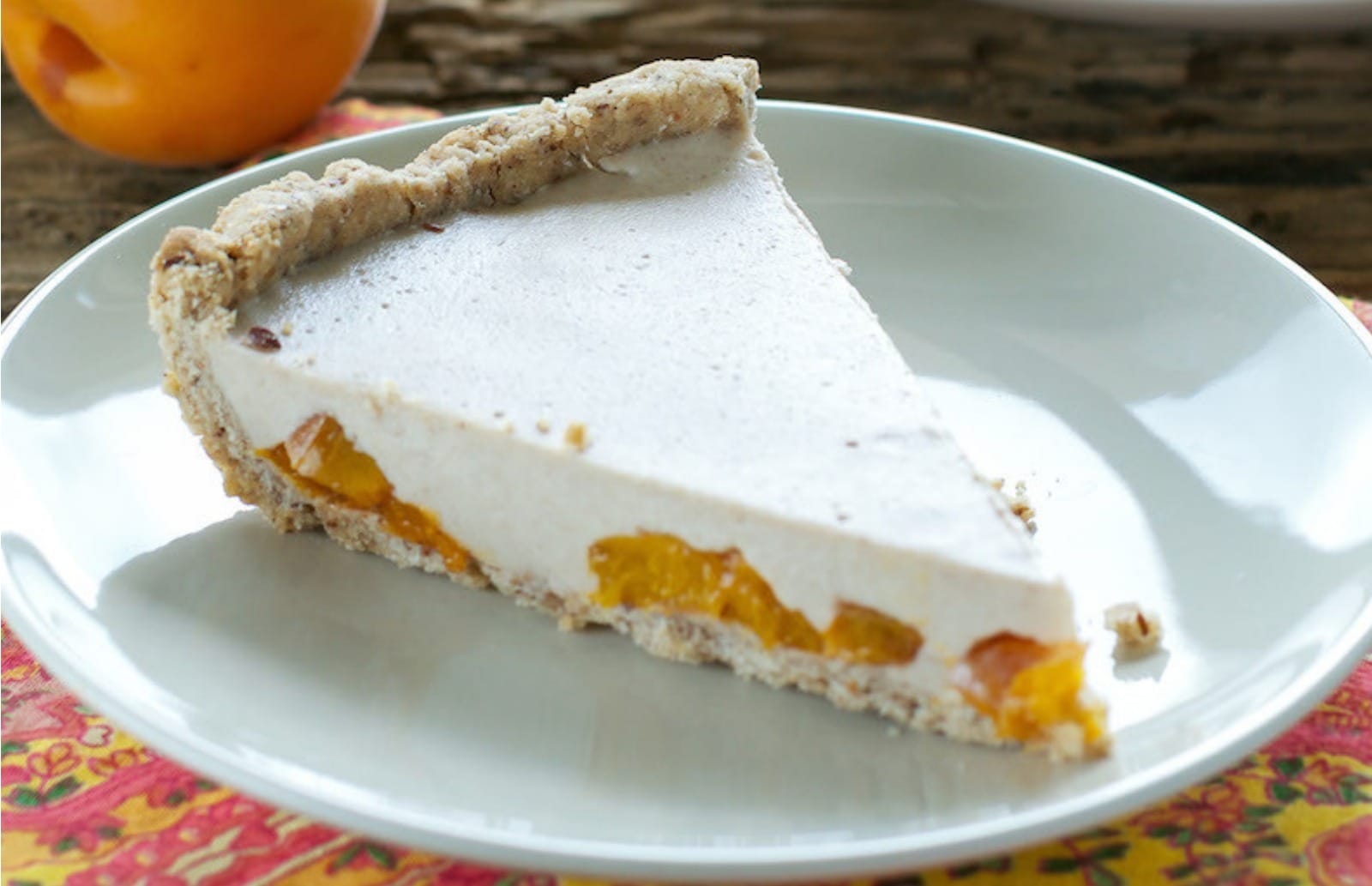 A slice of vegan Roasted Apricot Custard Pie showing the creamy, pale yellow custard filling with soft, golden-brown roasted apricot chunks, set in a pie crust on a white plate.