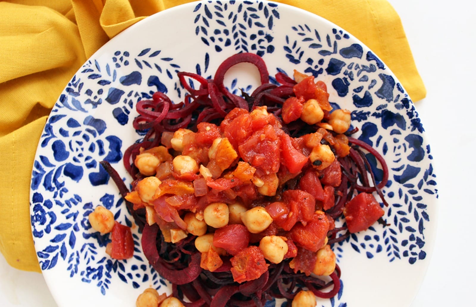A vibrant plate of Spicy Moroccan Chickpeas With Beet Noodles, featuring tender red beet noodles topped with a rich, spiced chickpea and apricot stew, garnished with fresh mint.