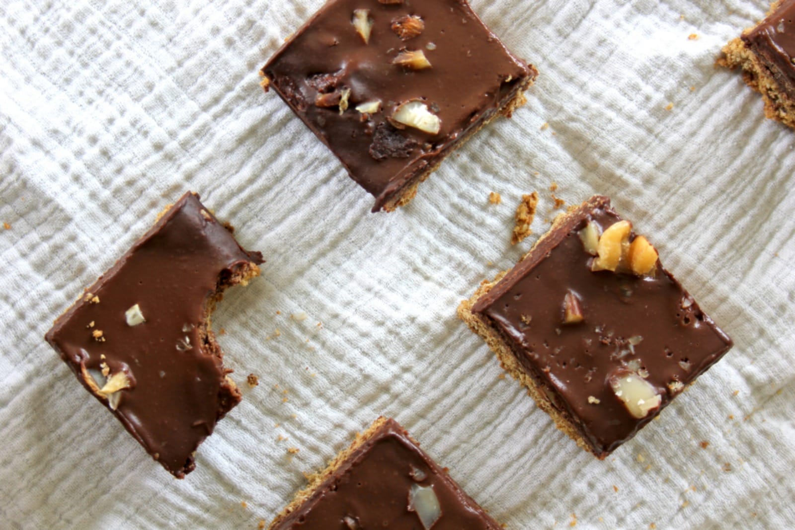 Sliced vegan shortbread brownies with a visible oat shortbread base, a rich chocolate brownie layer, and a smooth chocolate ganache topping, garnished with chopped nuts on a serving plate.