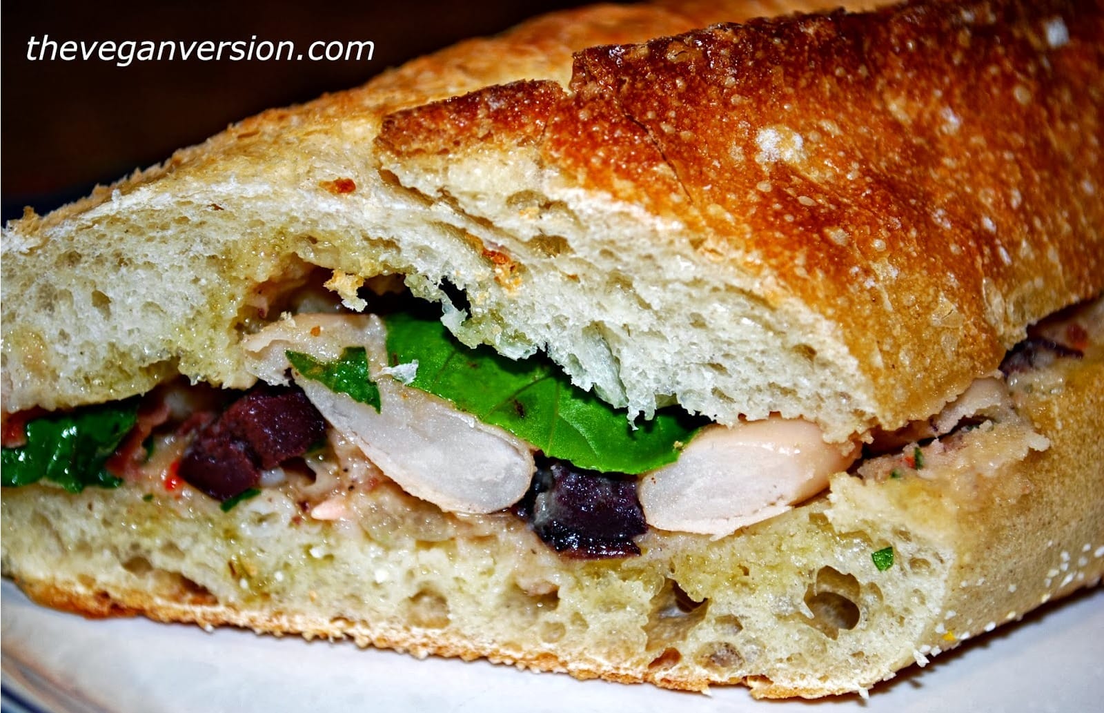 A sliced, pressed White Bean Nicoise Sandwich, showcasing mashed cannellini beans, kalamata olives, roasted red peppers, and fresh basil.