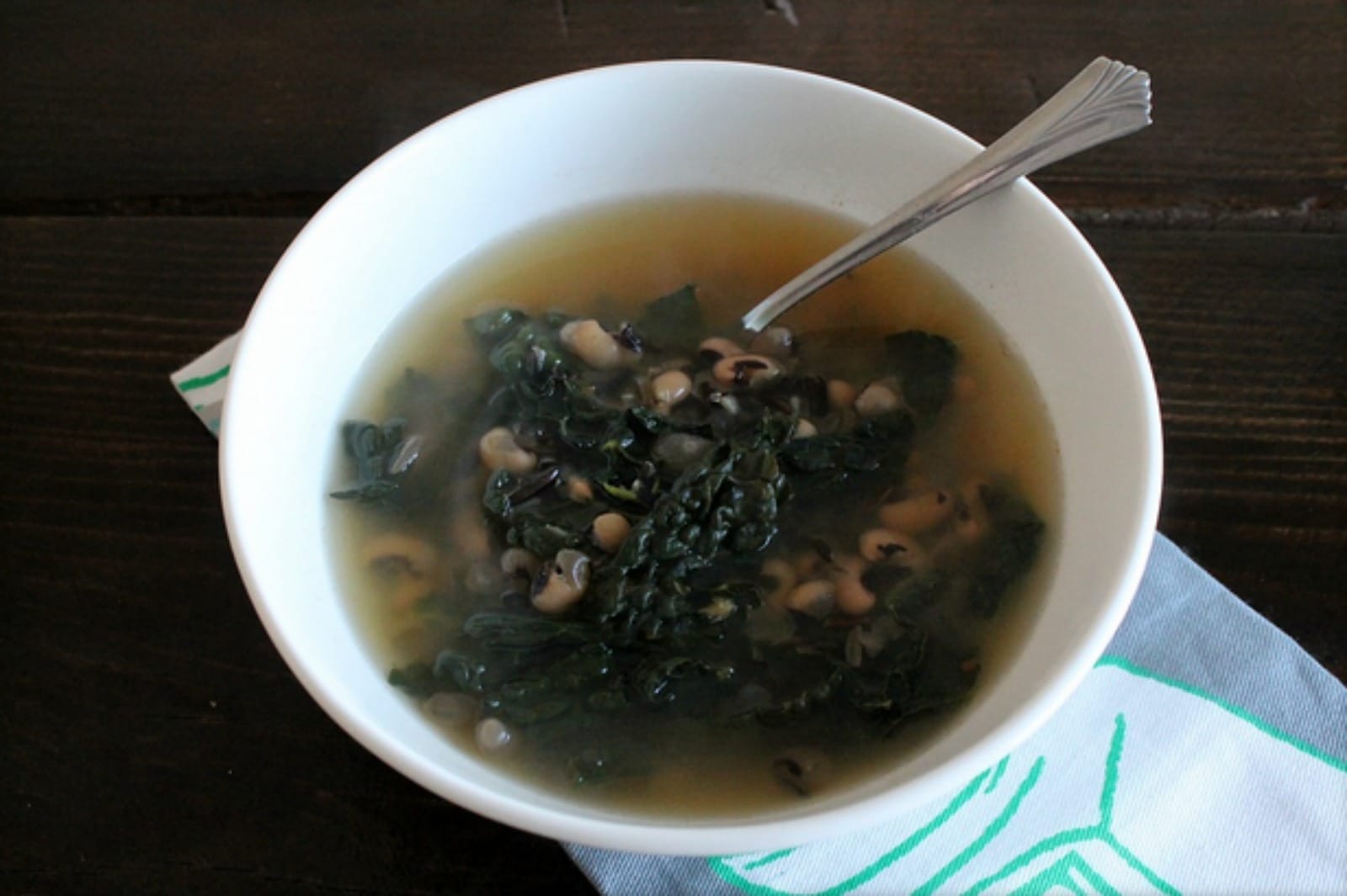 A steaming bowl of Black-Eyed Pea and Wild Rice Soup, garnished with fresh herbs, showcasing the dark black-eyed peas, chewy wild rice, and vibrant green kale.