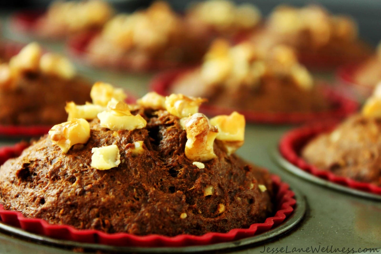 Warm vegan carrot gingerbread muffins, golden brown and spiced, with visible flecks of carrot and walnuts, served on a rustic plate.