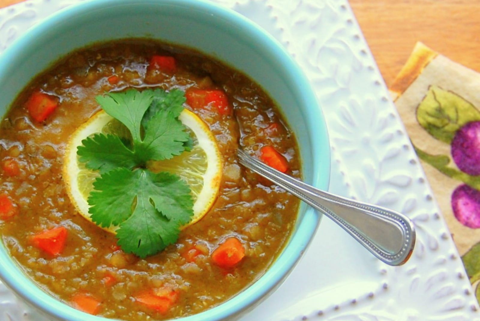 A vibrant bowl of thick red lentil soup garnished generously with fresh green chopped cilantro and bright yellow lemon wedges.
