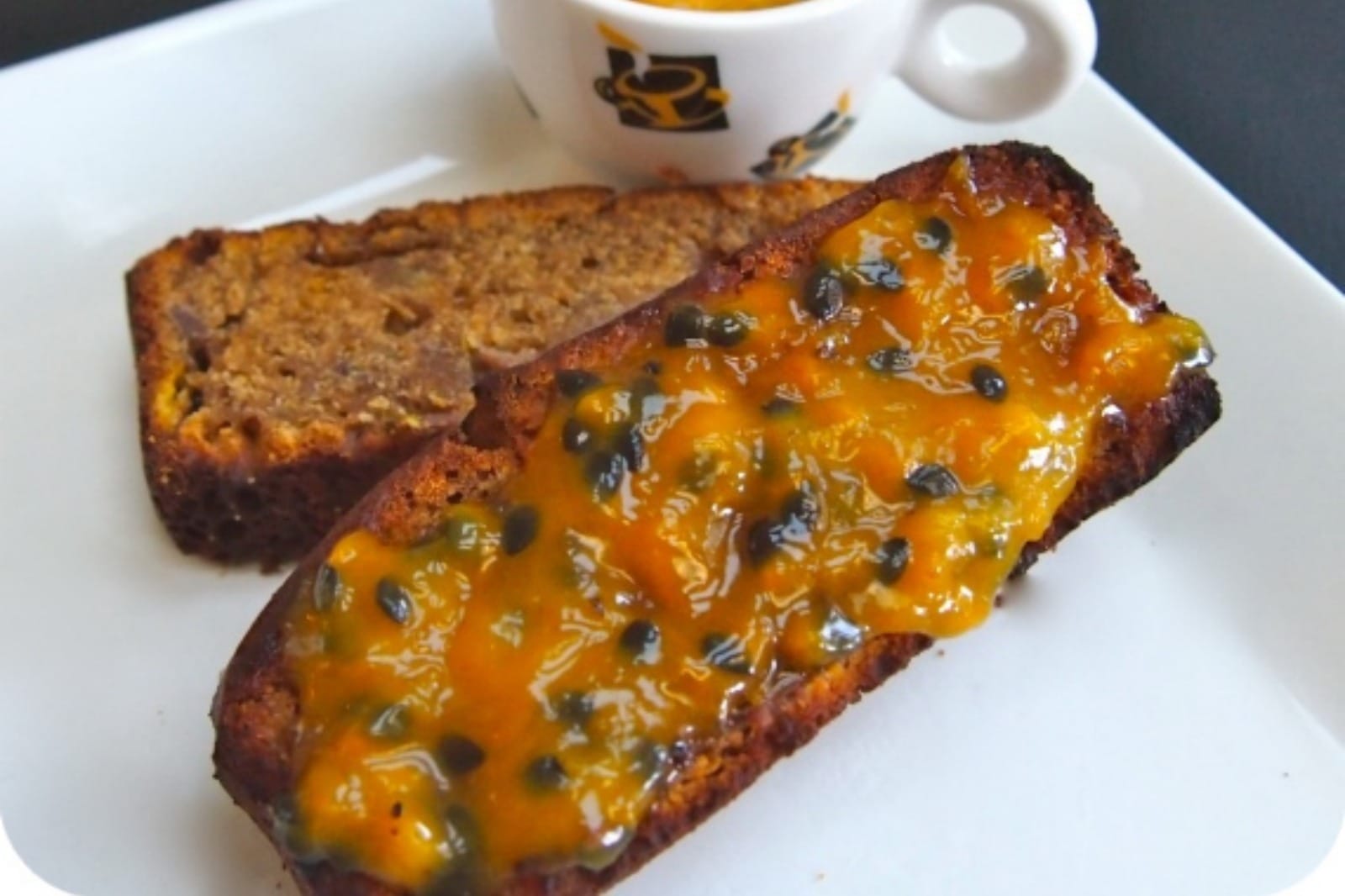 A slice of toasted vegan banana bread generously spread with vibrant yellow passion fruit butter, ready to be enjoyed.