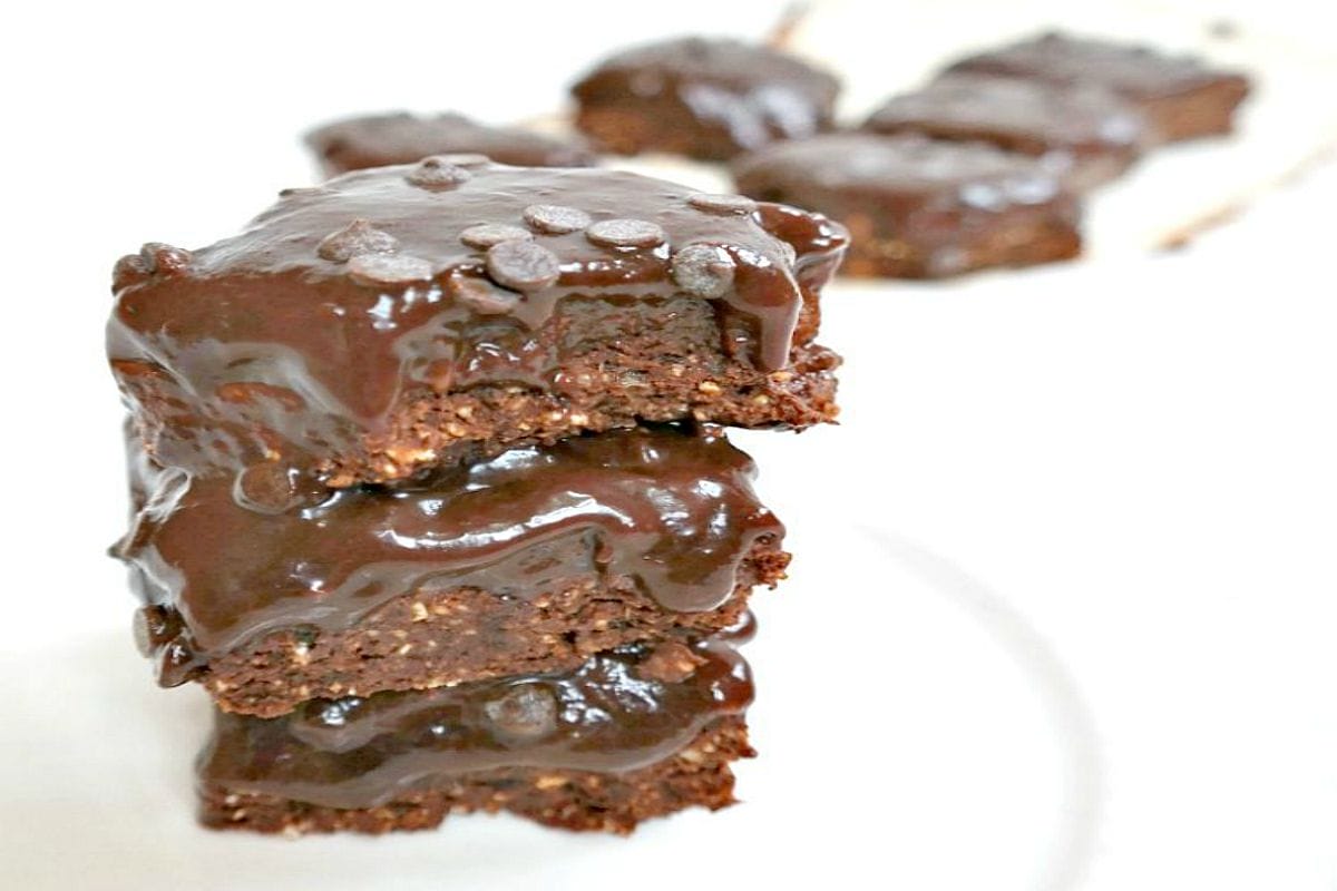 Sliced No-Bake Double Chocolate Brownie Bars, topped with vegan chocolate chips, arranged on a plate, showcasing their distinct crust and fudge layers.