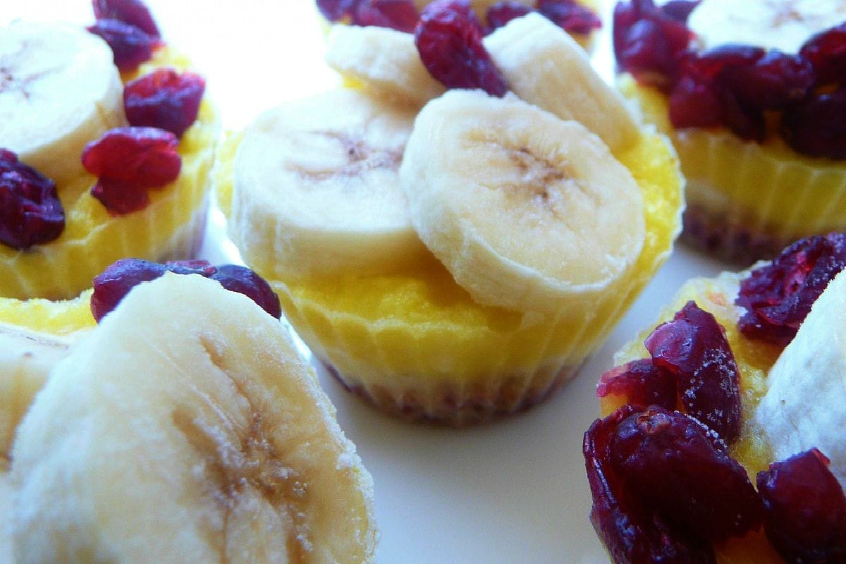 Six frozen Pineapple Paradise Cups in silicone liners, with visible layers of pecan-cranberry crust, banana, and pureed pineapple, garnished with cranberries.
