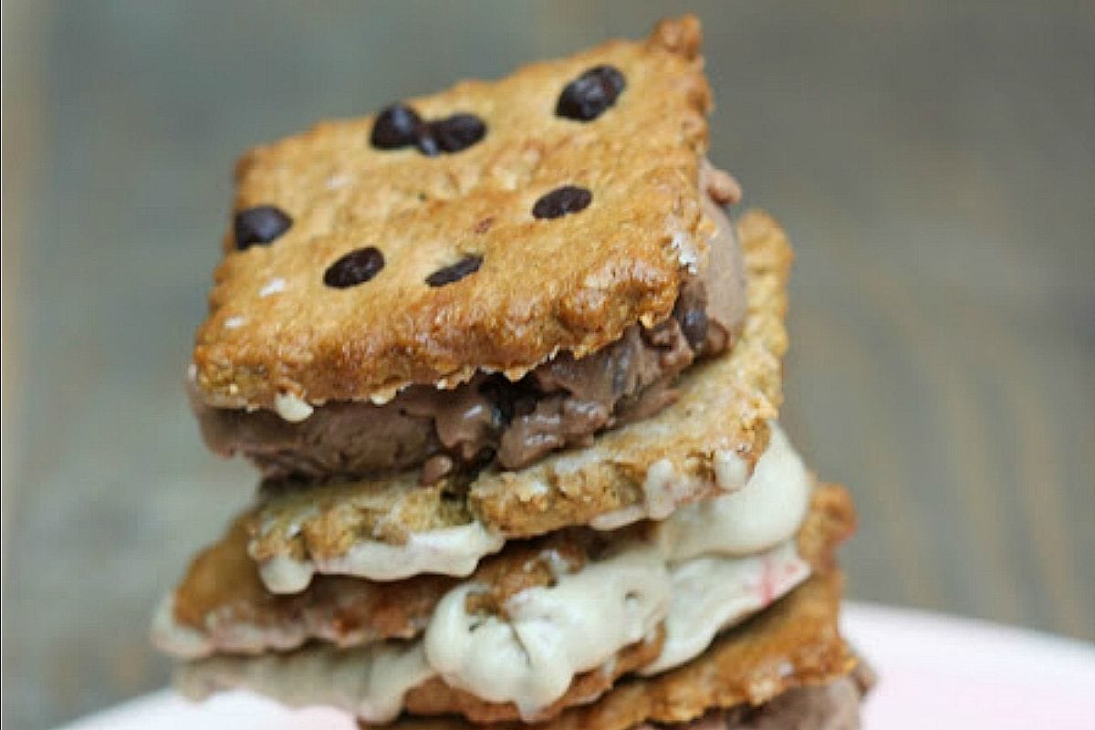 Two vegan ice cream sandwiches with creamy chocolate peanut butter and plain peanut butter ice cream fillings, sandwiched between crunchy chocolate chip cookies, presented on a white plate.