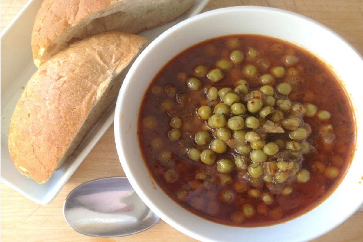 A close-up of a bowl of vibrant green Greek Peas (Arakas Kokinistos) in a rich red tomato sauce, garnished with fresh dill.