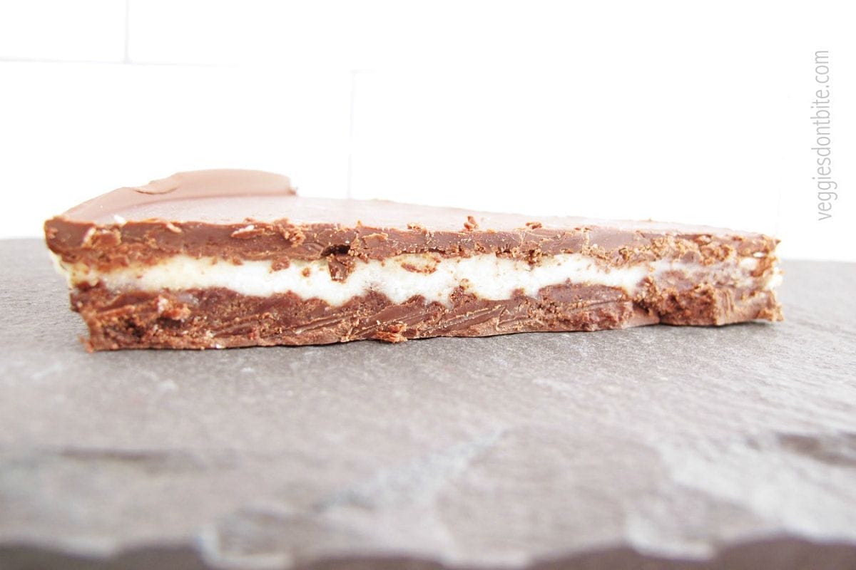 Plated slice of Frozen Chocolate Mint Pie showing dark chocolate cookie crust, light green cashew filling, solid chocolate topping, and mint garnish.