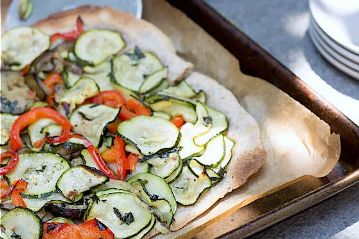 Close-up of a vibrant Summer Vegetable Flatbread Pizza with a golden cassava flour crust, topped with roasted eggplant, zucchini, red bell pepper, and fresh basil.