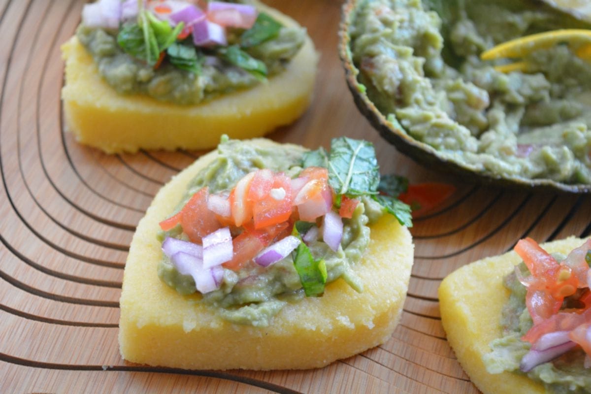 Pan-roasted Cheezy Polenta Bruschetta topped with creamy guacamole and a vibrant mint and coriander salsa, garnished with fresh herbs.