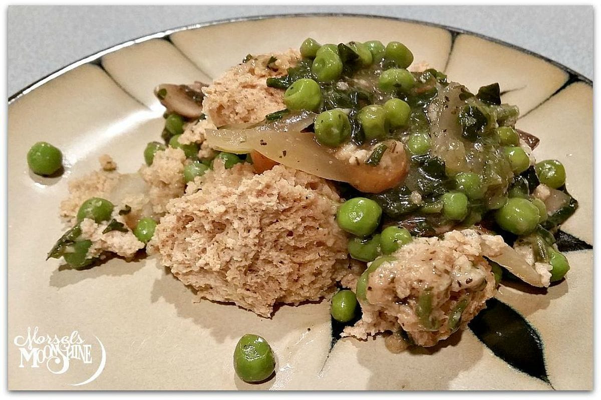 A steaming vegan Beer Broth Veggie Pot Pie in a ceramic dish, topped with golden-brown whole wheat biscuits, garnished with fresh parsley.