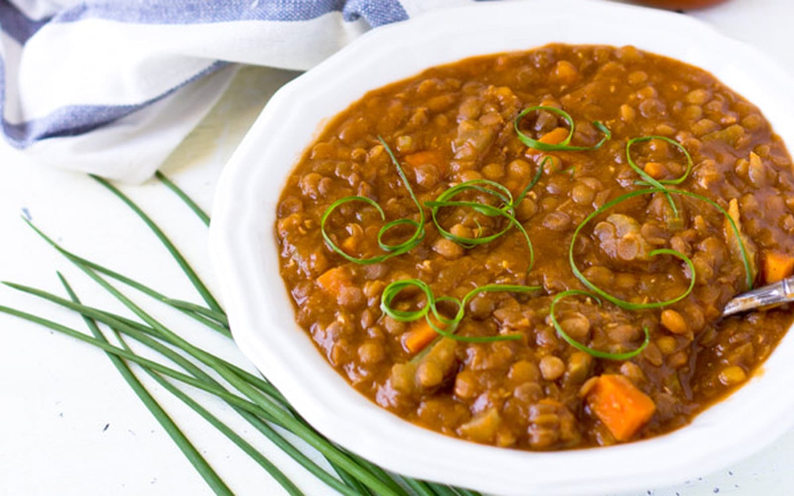 A bowl of hearty vegan barbecue lentil stew, garnished with chopped green onions, served warm and ready to eat.