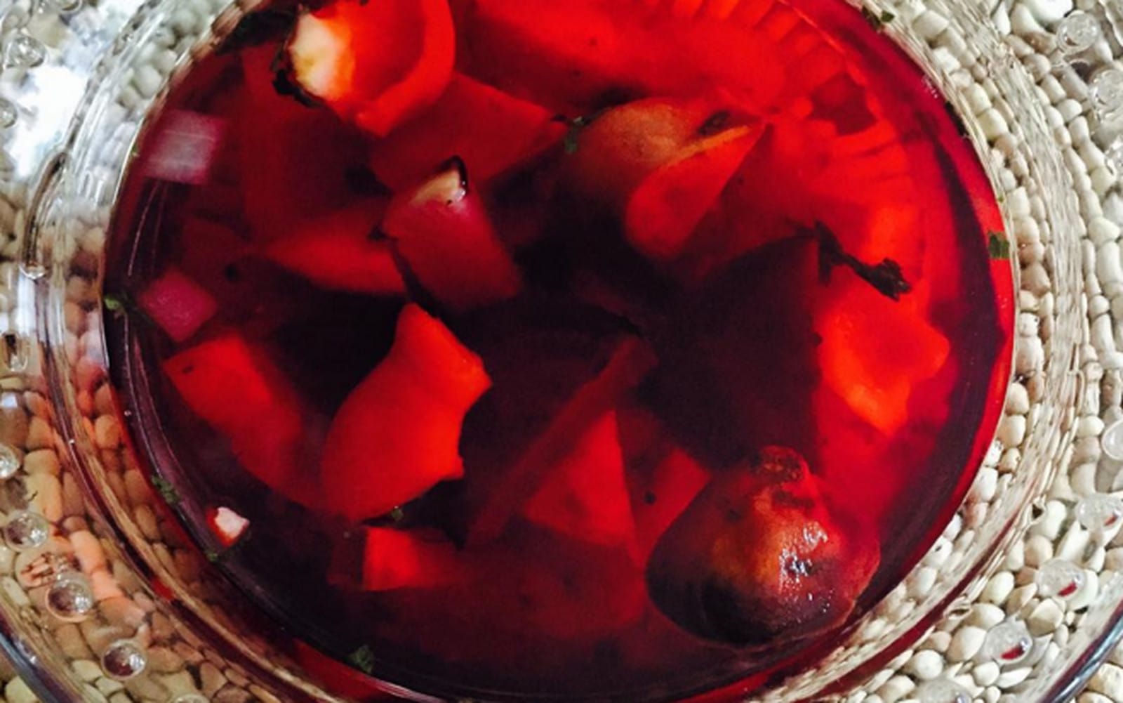 A vibrant bowl of Veggie Blood Soup, featuring a deep red broth with visible roasted sweet potato, beet, turnip, and fresh diced red onion and bell pepper, garnished with basil.