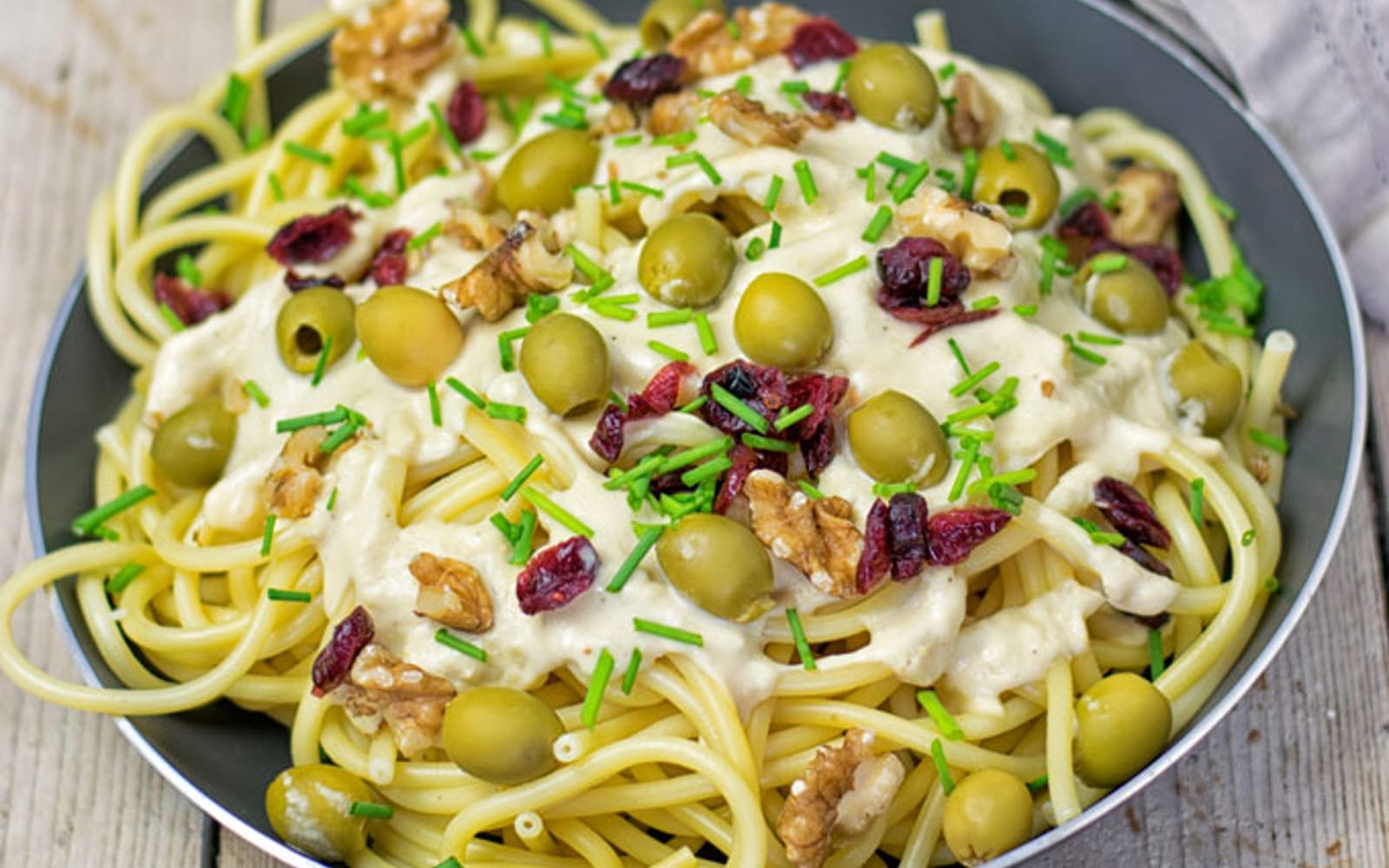 A vibrant bowl of 10-minute Mediterranean pasta, tossed with a creamy hummus sauce, green olives, walnuts, and a sprinkle of dried cranberries.