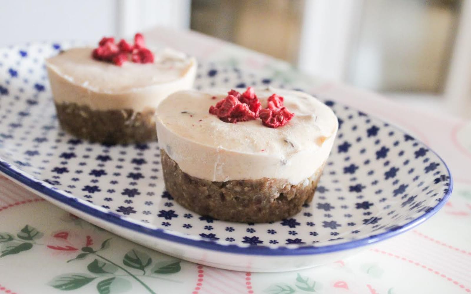 A close-up of several mini persimmon chestnut cheesecakes, topped with vegan chocolate chips and freeze-dried raspberries, served on a white plate.