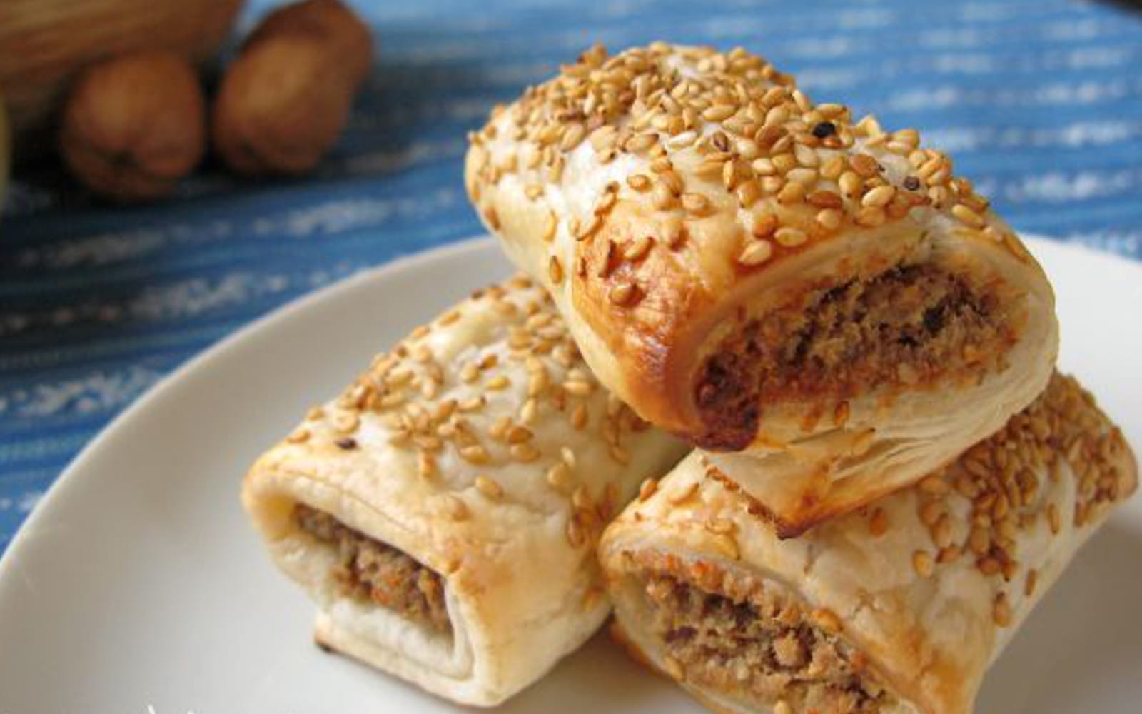 Golden brown vegan puff pastry sausage rolls, sprinkled with sesame seeds, arranged on a serving platter.