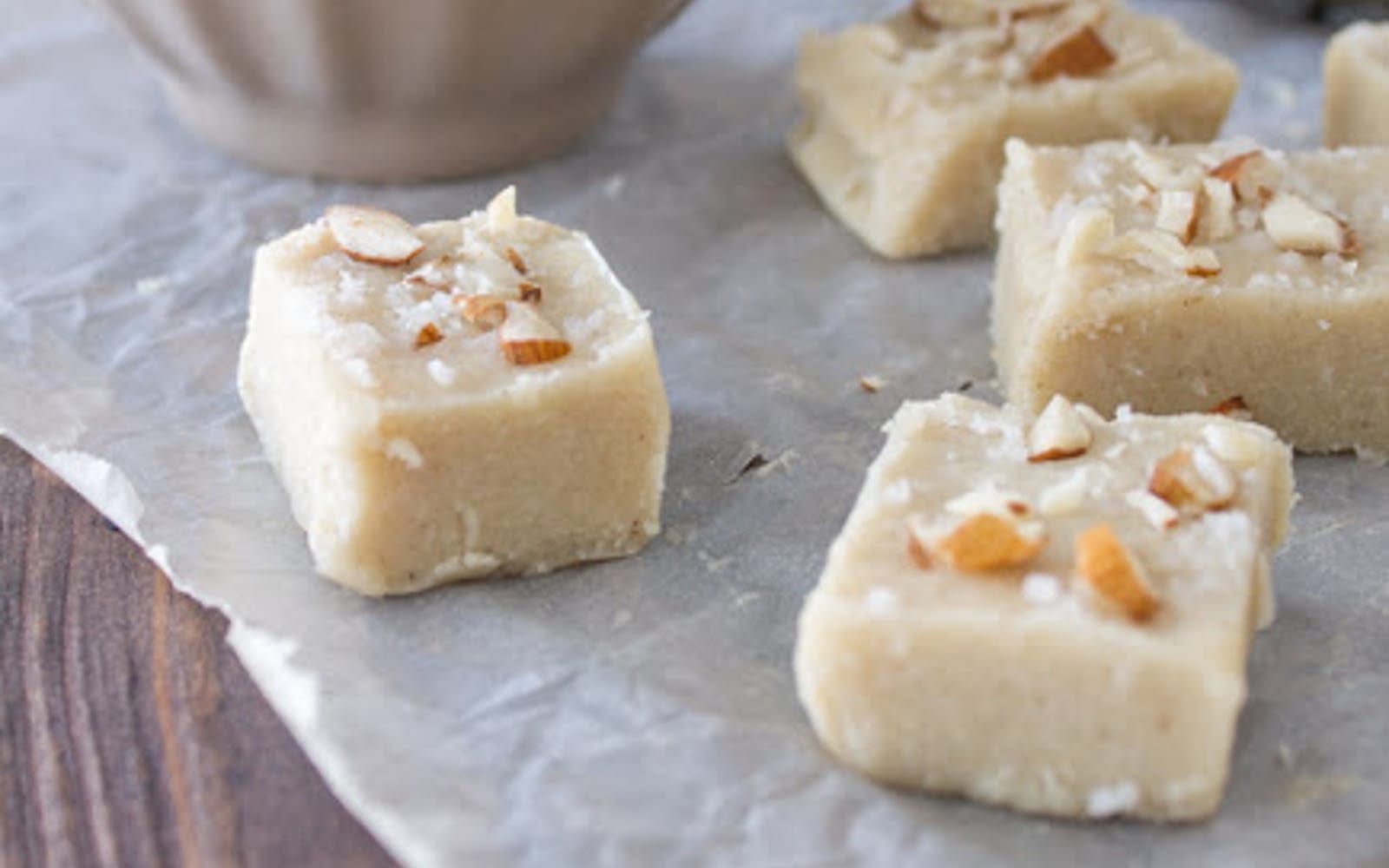 Square pieces of Tahini Coconut Fudge, topped with chopped almonds and a sprinkle of sea salt, arranged on a light surface.