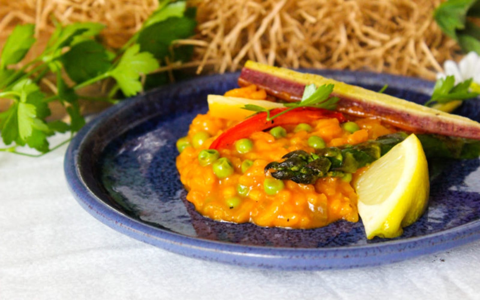 Golden Arborio rice risotto topped with vibrant roasted asparagus, red bell pepper, and carrot strips, garnished with fresh parsley and lemon.