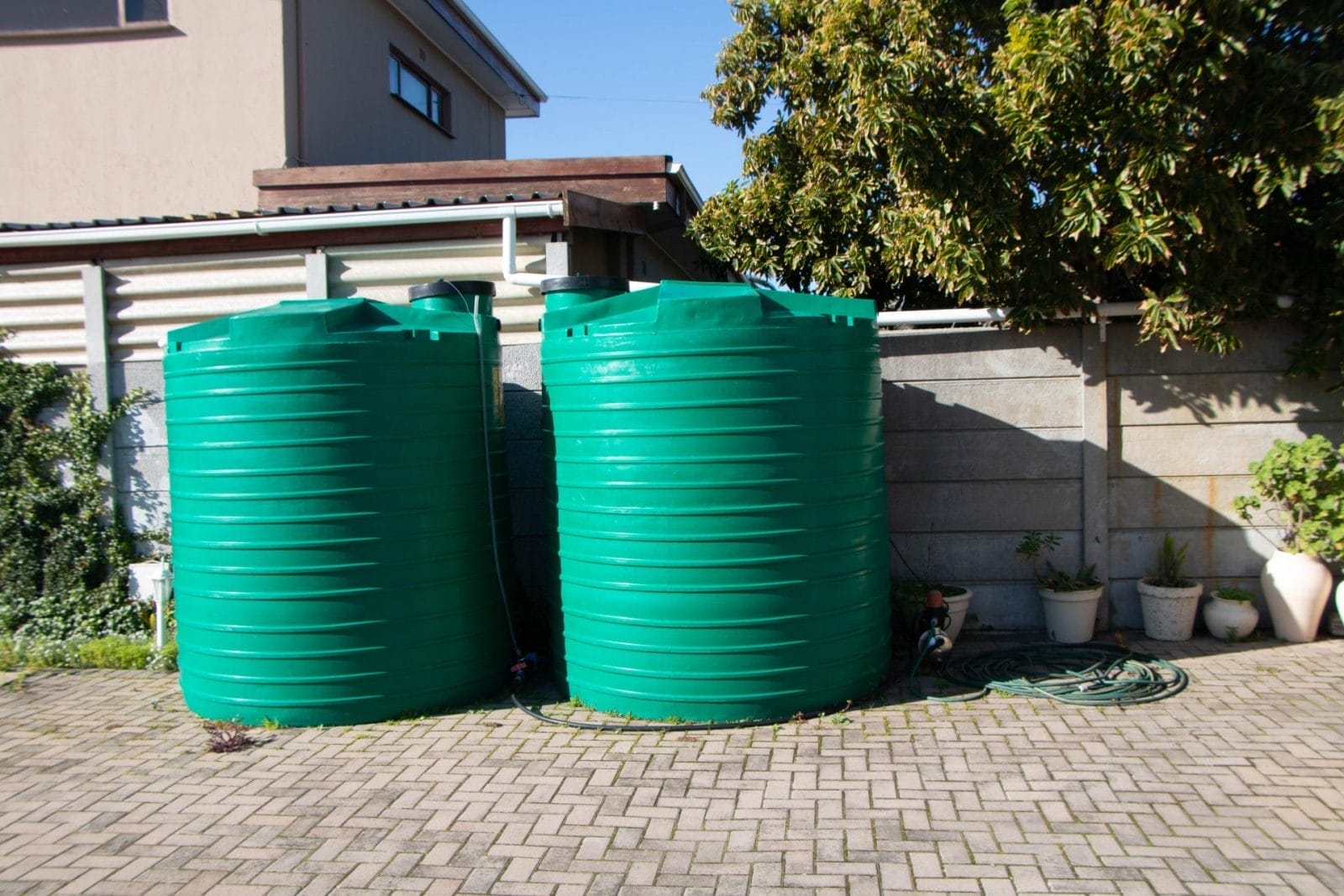rain barrel collecting roof runoff from a downspout beside a backyard garden
